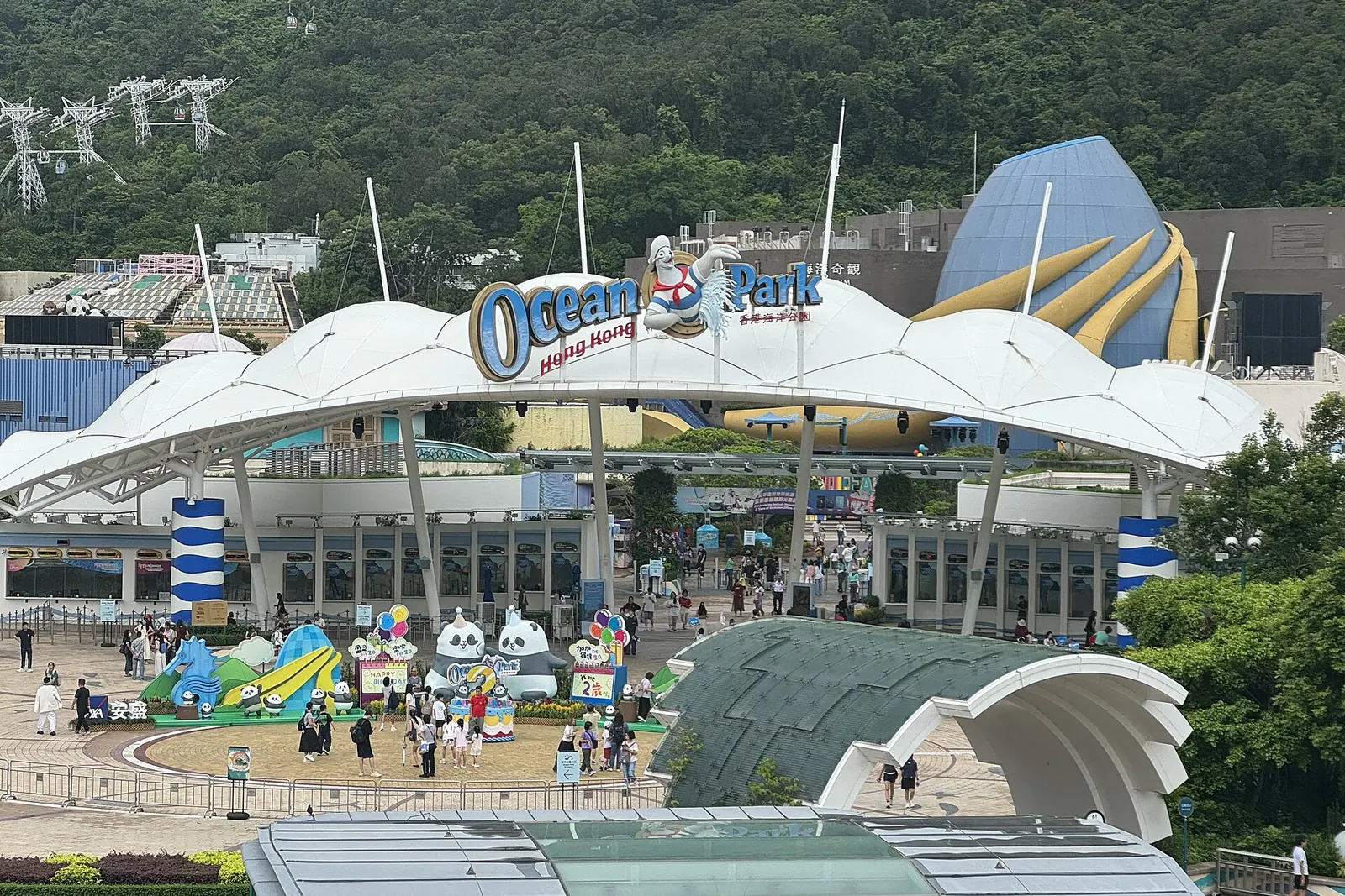 The white canopy of the Ocean Park main entrance with panda sculptures on the plaza and a blue dome behind