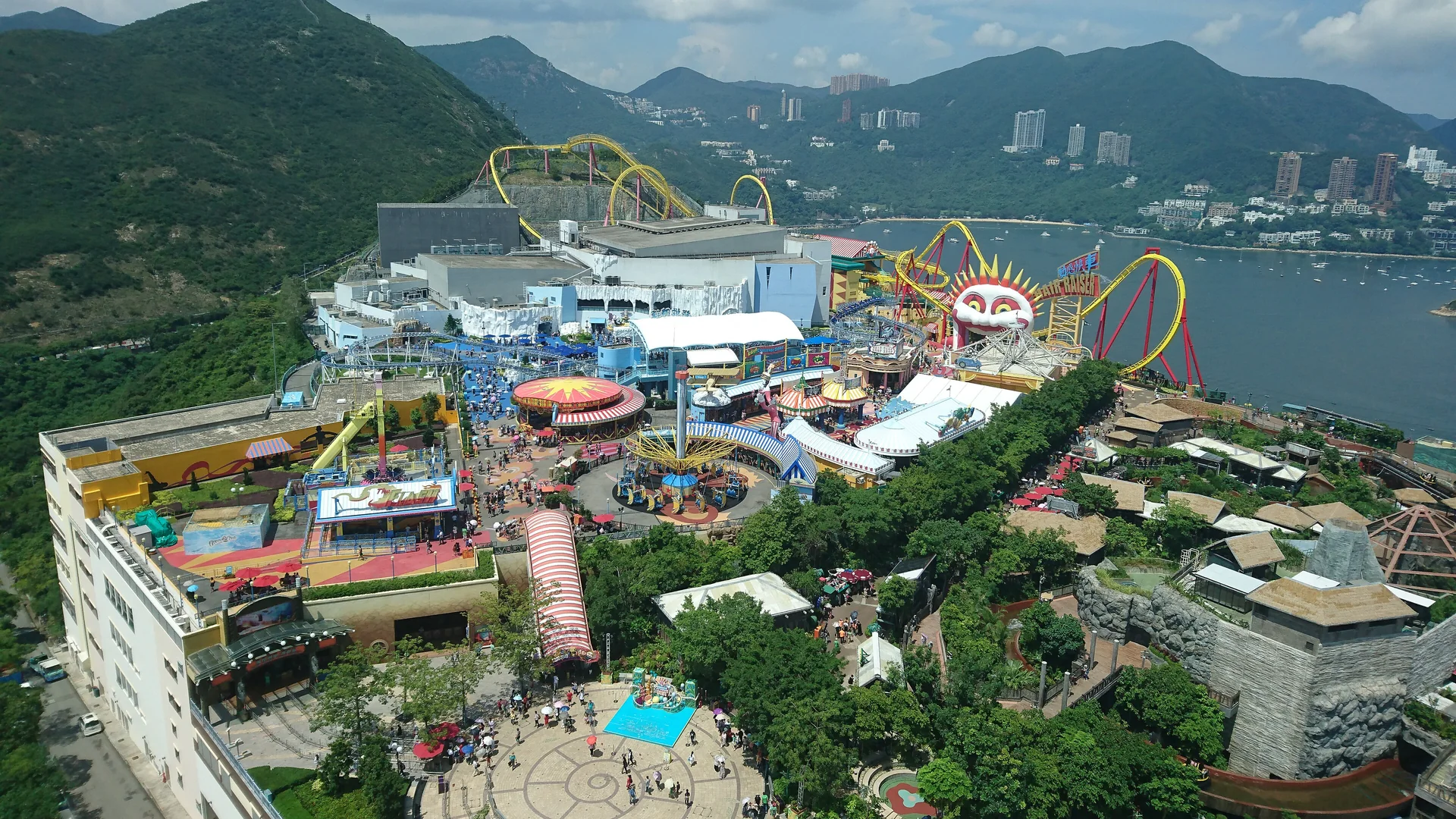 The Summit area of Ocean Park Hong Kong seen from above, with roller coasters beside a bay and green mountains behind